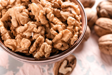 Bowl with tasty walnuts on color table, closeup