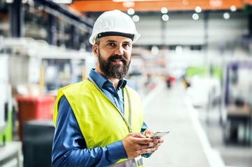 An industrial man engineer with name tag in a factory, using smartphone.