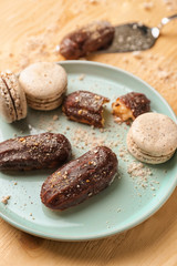 Plate with delicious eclairs and macarons on wooden table, closeup