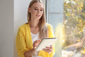 Beautiful young woman writing in notebook near window at home