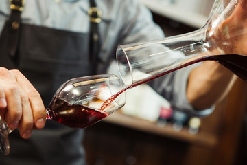 Sommelier pouring wine into glass from mixing bowl. Male waiter