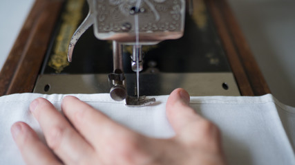 Sewing process. Foot of old vintage sewing machine and hands of elderly woman. Selective focus