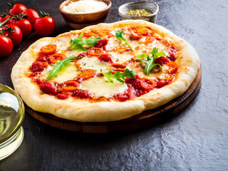 hot homemade Italian pizza margherita with mozzarella and tomatoes on dark brown stone table, side...