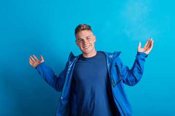Portrait of a young man with blue anorak in a studio, standing against blue background. © Halfpoint