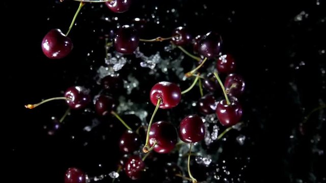 Whole and halves of cherry with water bouncing against to the camera on a black background in slow motion super close-up