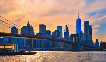 Naklejka na ściany i meble sunset on iconic manhattan modern architecture skyline with brooklyn bridge in Manhattan New York city with warm colors and cloudy orange sky