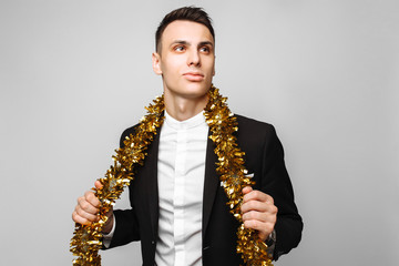 Naklejka premium attractive man in a business suit and with a tinsel around his neck, on a gray background.