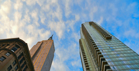 Fototapeta na wymiar Facade of classic old building with modern architecture and scyscrapers against cloudy blue sky, Manhattan,