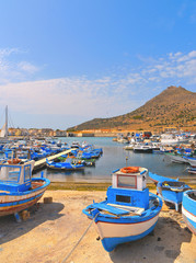 view of the port of Favignana with small fishing boats, typical houses and sea and mountains in background, Sicily Italy