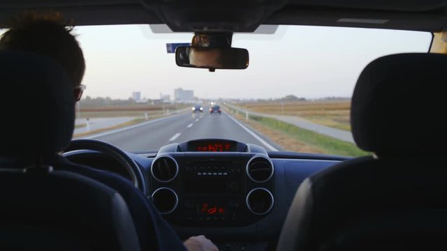 Backseat view of driving the car in slow motion 4K. Static long shot from car back seat with dashboard and windshield in focus with view on the road and oncoming traffic. 