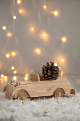 wooden car with pine cone on a wooden gray background and lights from the garland. Christmas concept