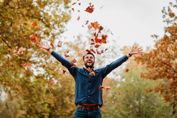 Young man throwing autumn leaves in the air