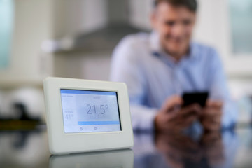 Man Controlling Central Heating Smart Meter Using App On Mobile Phone