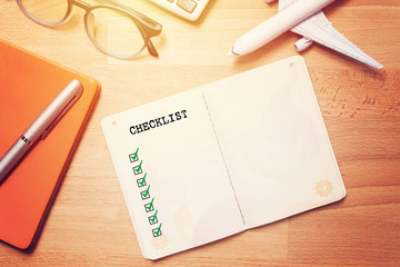travel checklist concept. notebook with blank checklist on wooden background with glasses and plane model