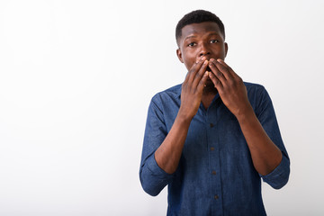Studio shot of young black African man looking shocked while cov