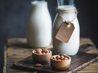 Two bottles of almond, gluten free milk and wooden bowls with almonds on rustic wooden table. Horizontal shot with copy space.