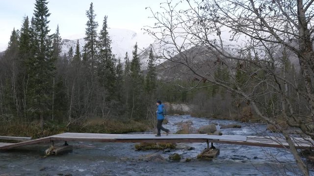 A man traveler crosses a mountain stream over a bridge. Beautiful view.