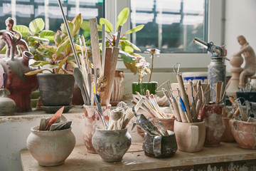 selective focus of pottery tools and paintbrushes at table in pottery studio - obrazy, fototapety, plakaty