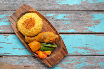 Top view of Malay traditional food called 'Nasi Minyak' with colorful rice, red chili ,spicy sauce, chicken, cucumber, carrot, and potato on the wooden plate.