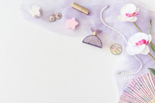 Beauty products, decorative cosmetics top view on white background. Flat lay for fashion blogger. Copy space. Lipstick, Lilac scarf, Bottle, bijou, Pearl Beads and Orchid Flower on a White Background