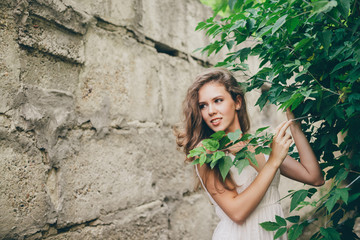 Beautiful happy girl with curly natural hair in white dress near green tree leaves. Summer beauty portrait. Dreamer lady enjoy nature. Inspired woman with dreamy sight in long tunnel in forest.