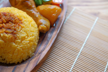 Top view of Malay traditional food called 'Nasi Minyak' with colorful rice, red chili ,spicy sauce, chicken, cucumber, carrot, and potato on the wooden plate.