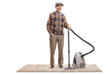Senior man standing with a vacuum cleaner on a carpet