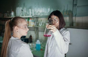Two young woman in chemical laboratory holding a flask with pink liquid in it