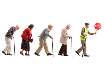 Senior people walking in a line behind an elderly man with a safety vest and stop sign