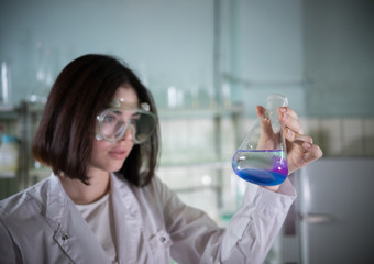 Chemical laboratory. Young woman holding a flask with blue and purple exfoliating liquid in it....