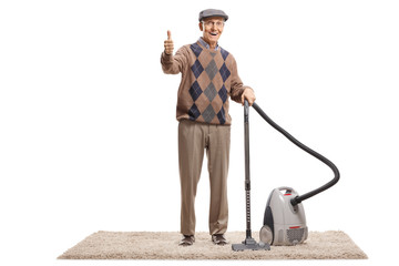 Senior man standing with a vacuum cleaner and showing thumbs up