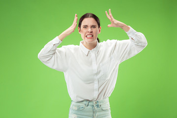 Fototapeta premium Angry woman looking at camera. Aggressive business woman standing isolated on trendy green studio background. Female half-length portrait. Human emotions, facial expression concept