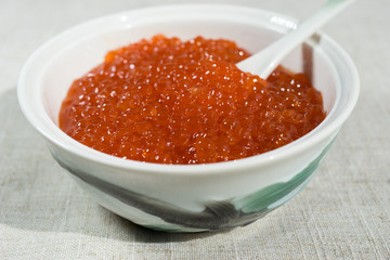 Large red caviar in a beautiful porcelain icon on a gray tablecloth.