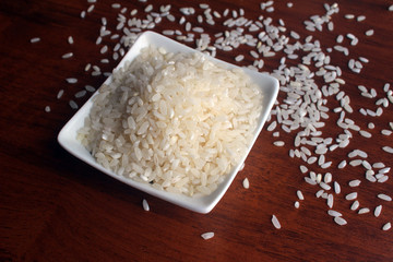 White Bowl with grains of white rice on a wooden table, top view. Randomly scattered grains around the bowl. Photo with empty place for text.   