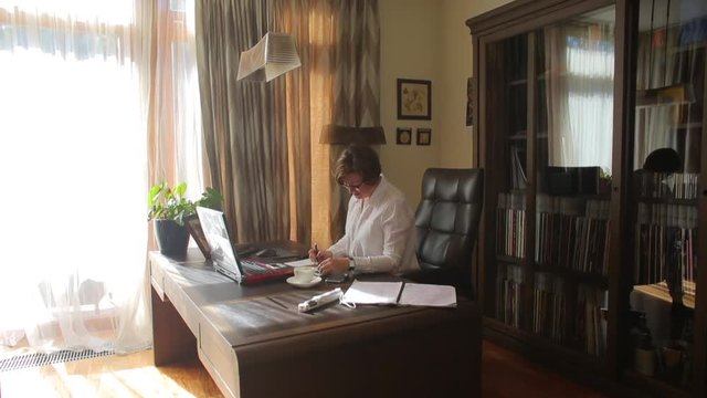 A woman writes in a notebook at her desk in her home office. Home Office. Remote work online. Adaptation of people to coronavirus. Quarantine COVID 19.  