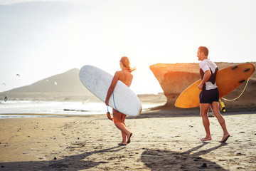 Surfers couple running together with surfboards on the beach at sunset - Sporty friends having fun...