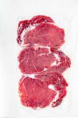 Fresh raw beef steaks  in   transparent vacuum packed   isolated on white background, top view