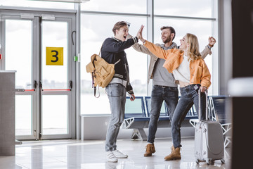 happy young friends giving high five in airport terminal