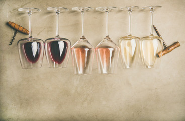 Flat-lay of red, rose and white wine in glasses in row and corkscrews over grey concrete background, top view, wide composition. Wine bar, winery, wine degustation concept