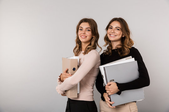 Image of two teenage women smiling and holding folders, isolated over gray background