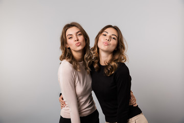 Image of two gorgeous girls smiling and posing together, isolated over gray background