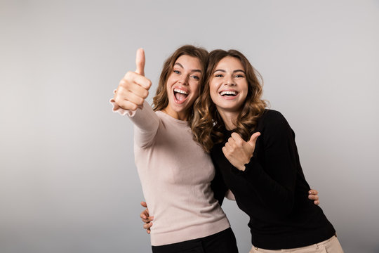 Image of two happy women smiling and showing thumbs up, isolated over gray background
