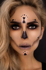Sexy blonde woman in Halloween makeup and leather outfit on a black background in the studio....
