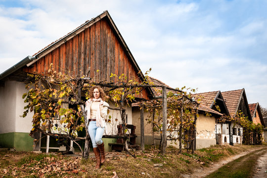 Beautiful curly woman standing next to a house on brown leaves during autumn on a vineyard