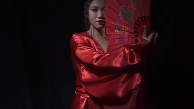 Geisha in a red dress lifts up a fan and covers half of the face