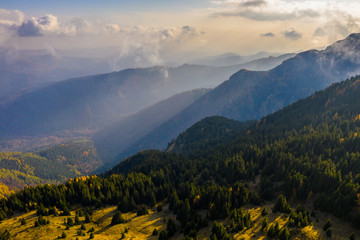 Fototapeta premium Aerial photography over big mountain forest. Sunset over the forest. Foggy valley at the sunrise. Golden hour over the forest with mist. Beautiful aerial landscape. Drone shots over the foggy forest. 