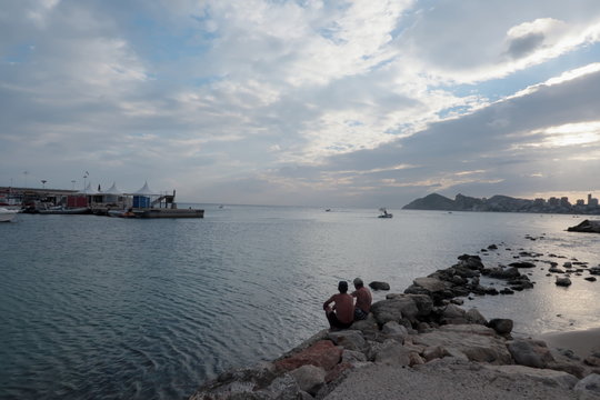 Mediterranean sea landscape at sunset. It is at night on the beach, next to Benidorm's marina and fishing port and the buildings at the bottom of Poniente beach, the cloudy sky with clouds illuminated