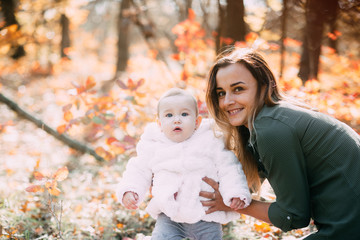 Young mother with little girl in autumn forest with a beautiful colored background