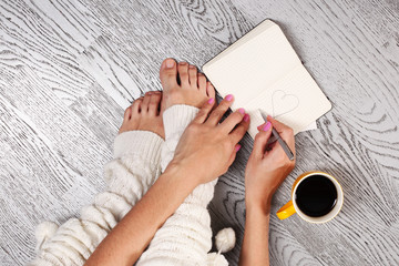 Woman's legs in white gaiters draws a heart in notebook, top view