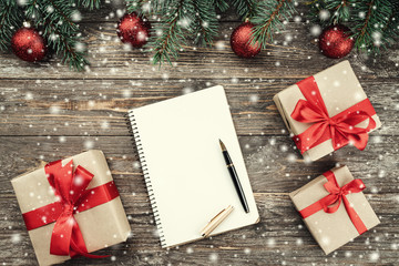 Old wood background with fir branches adorned with baubles. Holiday Gifts. Congratulation message notebook. Christmas card. Top view. Effect snowflakes.